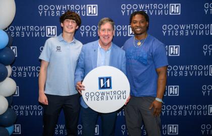 Two honors students pictured with President Kent MacDonald. Northwood University backdrop and balloons while Kent holds a white circle sign with the Northwood University logo.